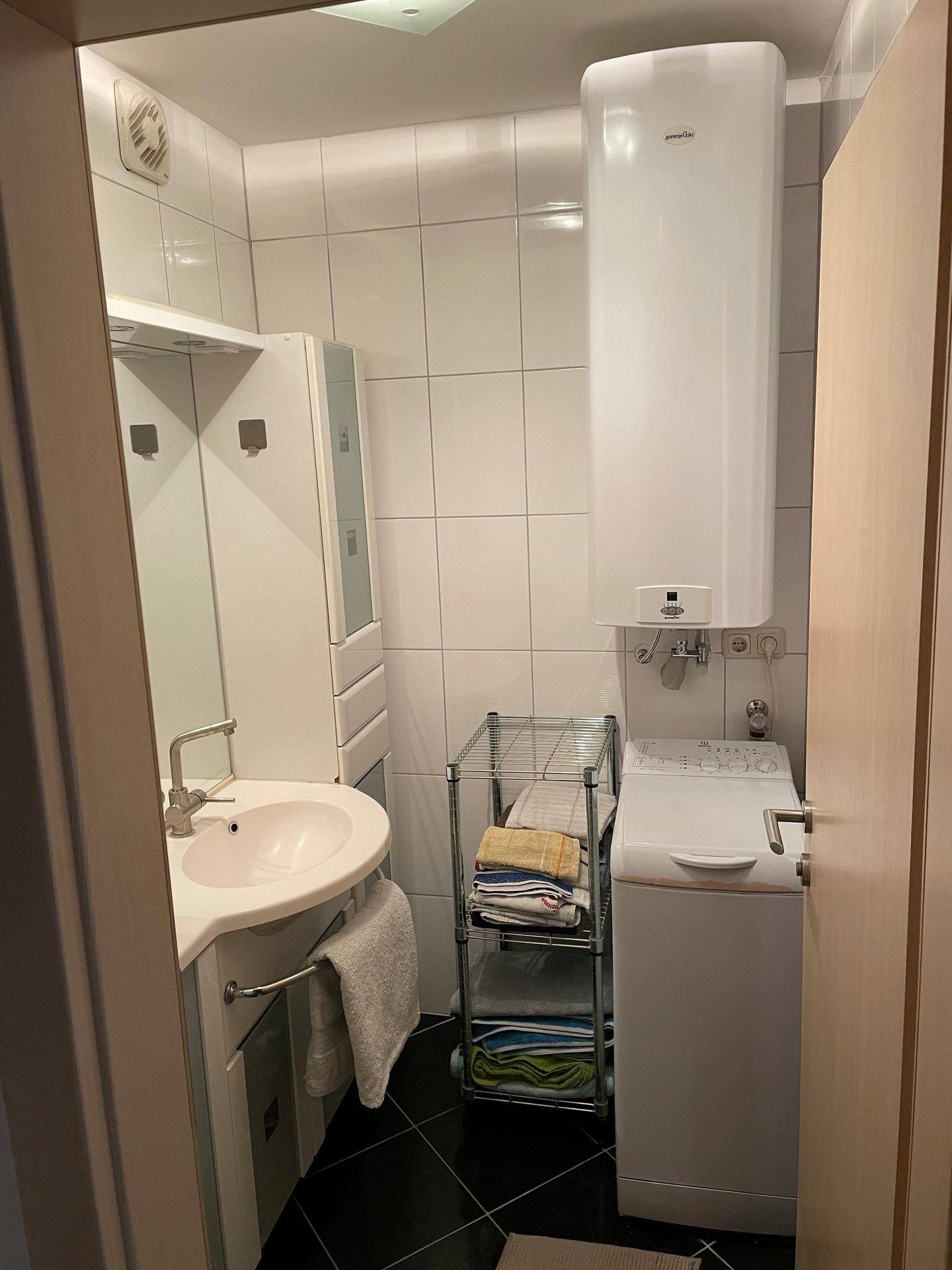 Badezimmer mit Waschbecken, Waschmaschine und Warmwasserboiler, praktisch eingerichtet.