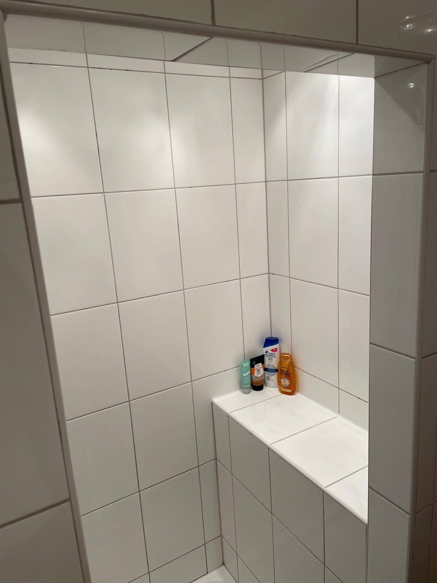 Moderne Duschkabine mit weißen Fliesen und integrierter Sitzbank, bietet Komfort.