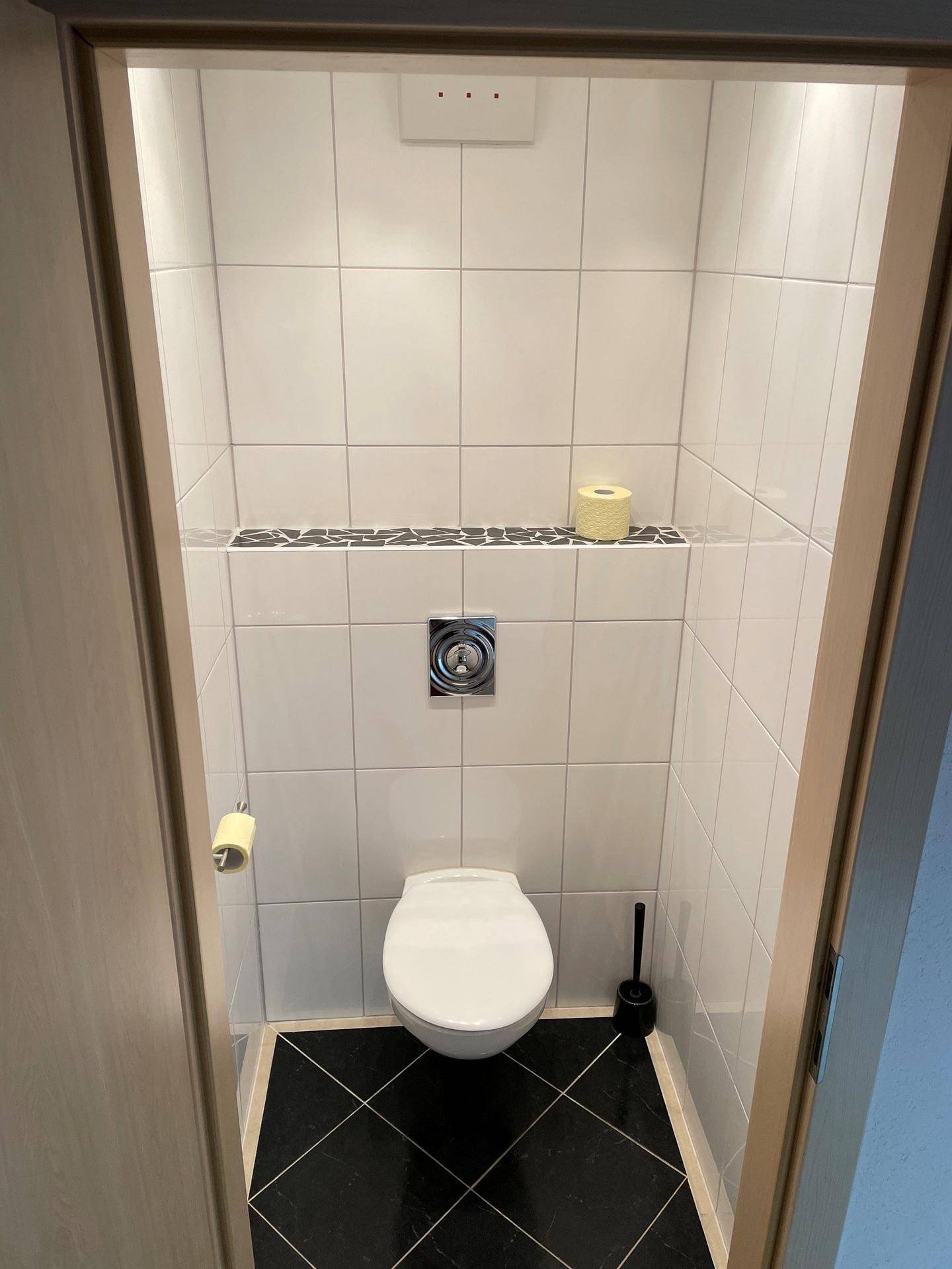 Separates WC mit wandmontierter Toilette und schwarzen Bodenfliesen, minimalistisch gestaltet.