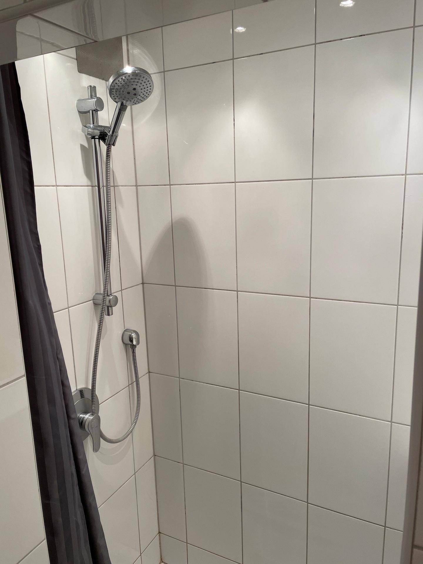 Duschbereich mit Handbrause und weißen Fliesen, sauber und funktional.