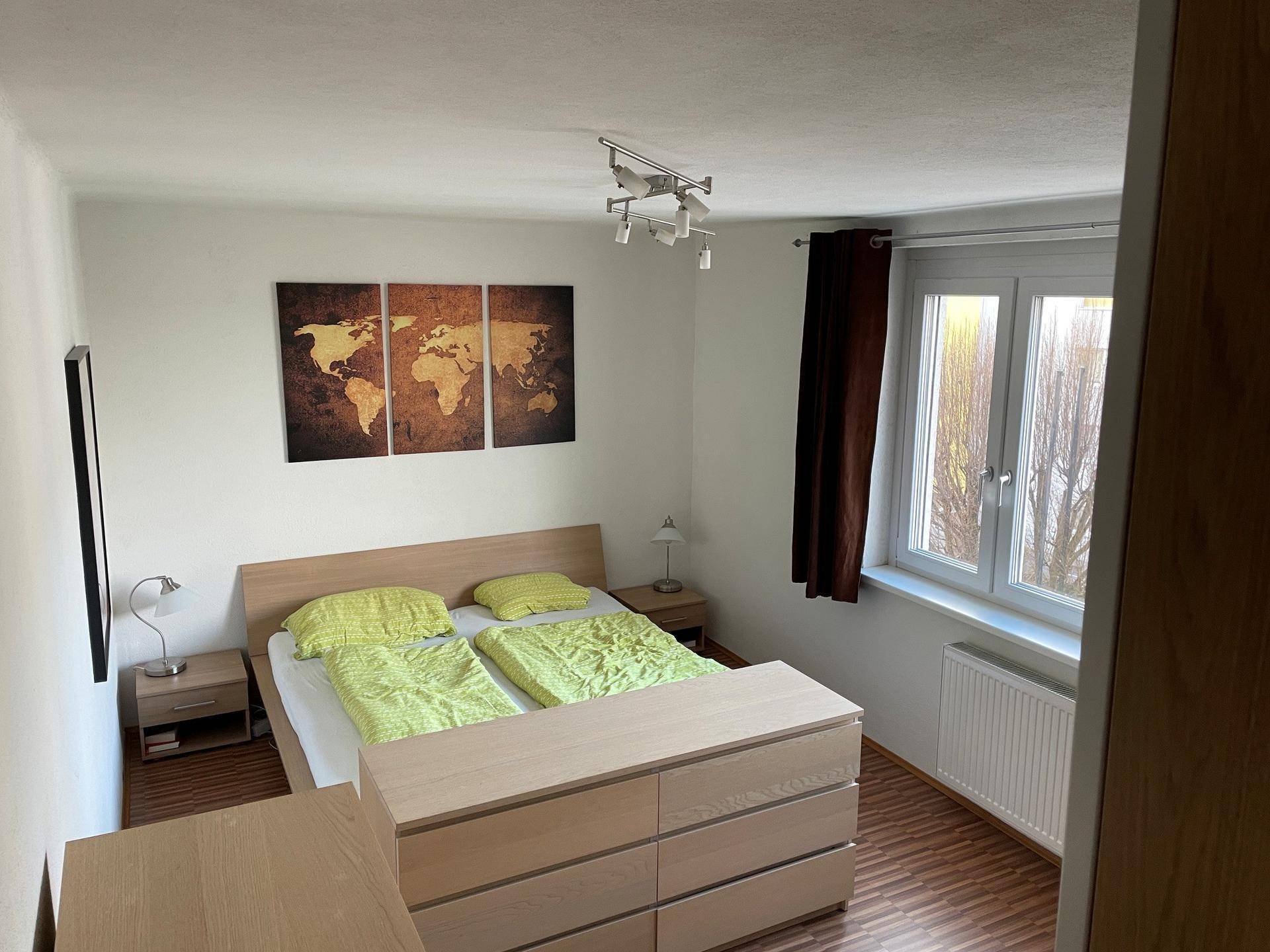 Schlafzimmer mit Doppelbett, Nachttischen und Fenster, das für natürliches Licht sorgt.