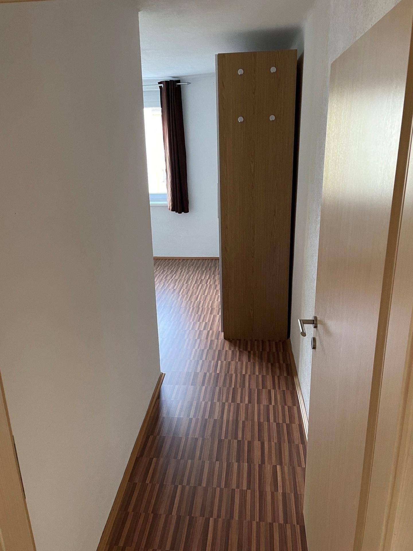 Schmaler Flur mit Laminatboden, der zu einem weiteren Raum mit Fenster führt.