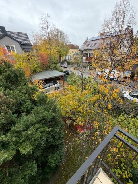 Balkon mit weitem Blick auf die grüne Umgebung und Nachbarhäuser, mit Carport im Hintergrund.