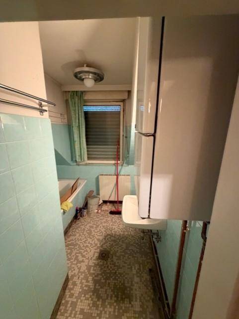 Badezimmer mit hellblauen Fliesen, Badewanne, Waschbecken und einem Fenster.