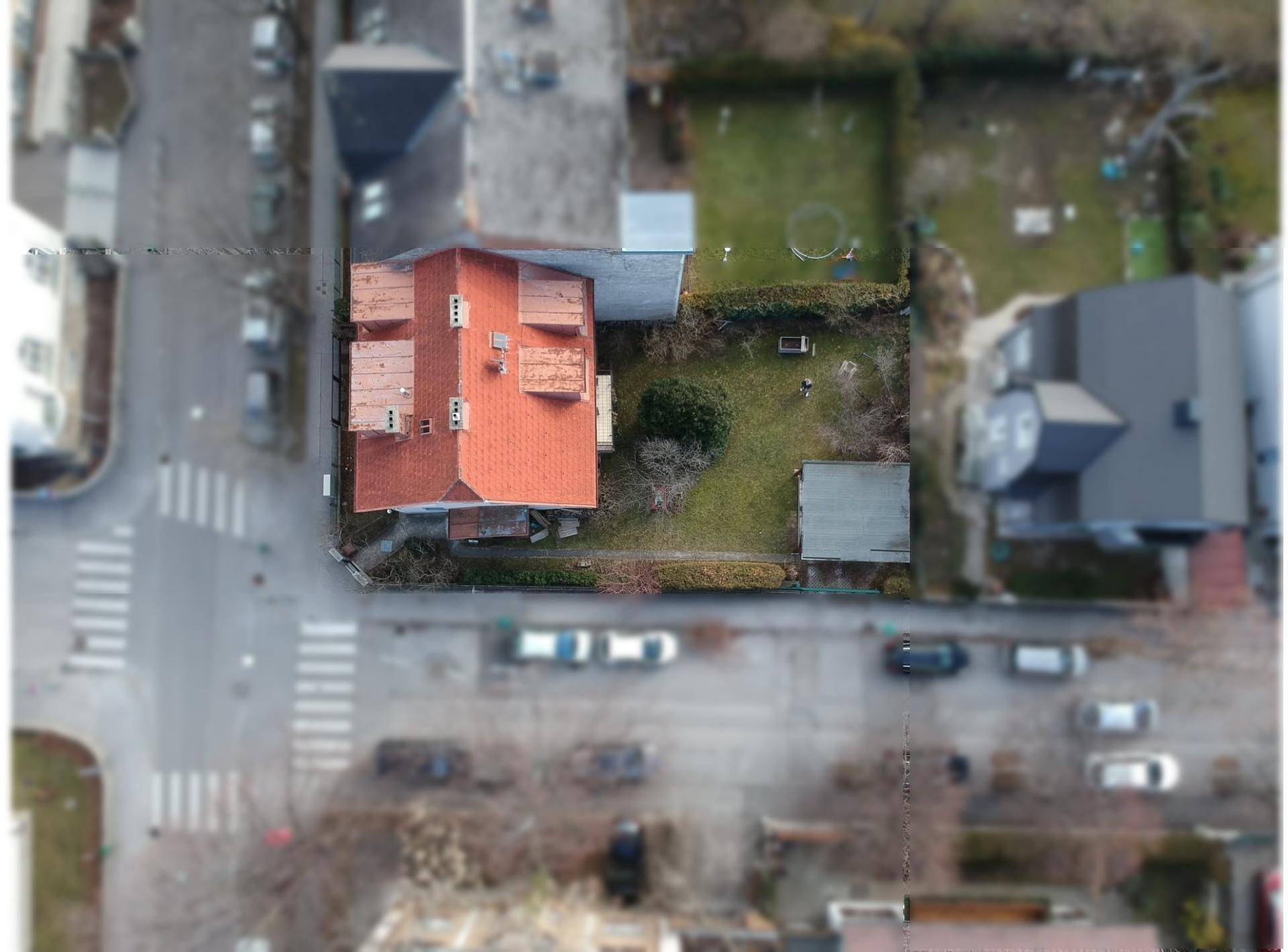 Luftaufnahme des Wohnhauses mit rotem Ziegeldach und angrenzendem Gartenbereich in städtischer Umgebung.