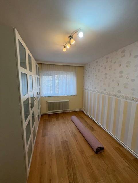 Schlafzimmer mit Holzboden und großem Fenster, vielseitig nutzbar, mit weißem Schrank.
