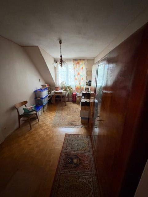 Dachzimmer mit schrägen Wänden, Parkettboden und einem Fenster mit Vorhängen.