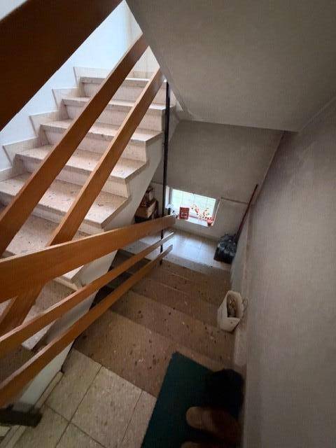 Treppenhaus mit Holzgeländer und Terrazzoboden, führt zu den oberen Etagen des Hauses.