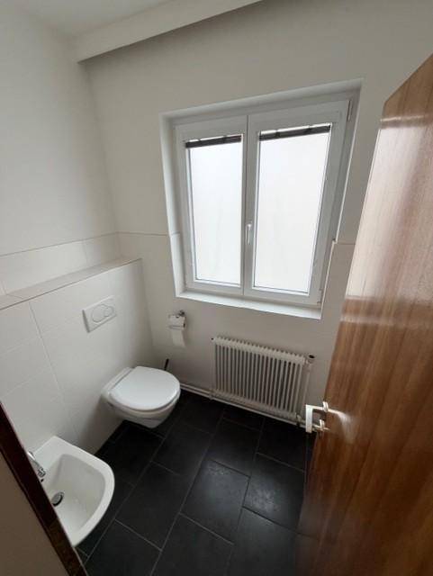 Separate Gästetoilette mit Fenster, WC und Bidet, sauber und funktional, mit dunklem Fliesenboden.