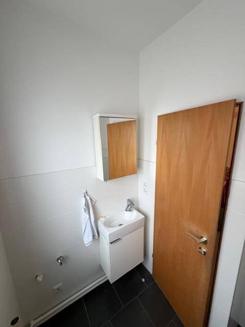 Kleine Gästetoilette mit Waschbecken und Spiegelschrank, praktisch eingerichtet, mit dunklem Boden.