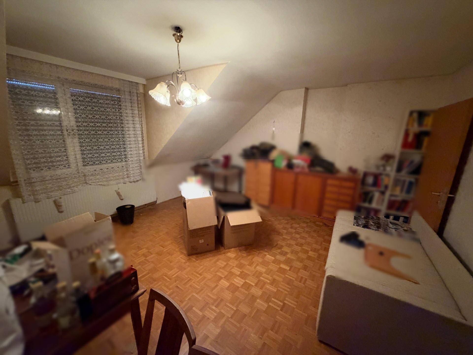 Helles Dachzimmer mit Parkettboden, schrägen Wänden und einem Fenster.