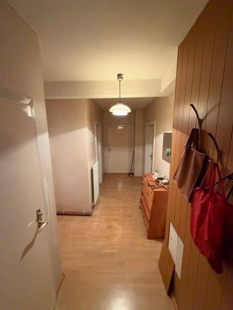 Langer Flur mit hellem Parkettboden und Holzverkleidung an einer Wand.