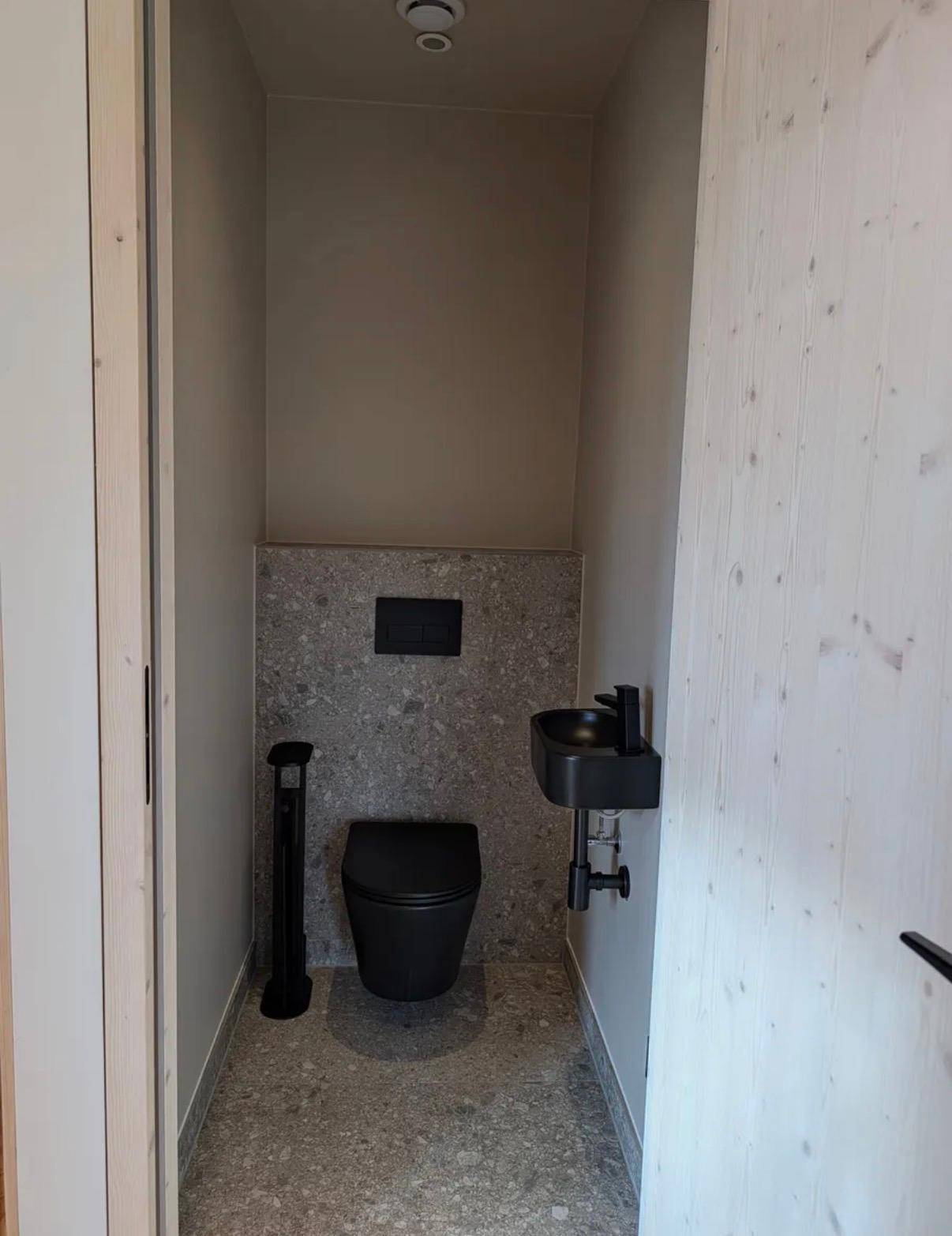 Modernes Gäste-WC mit schwarzer Toilette, kleinem Waschbecken und grauen Fliesen.