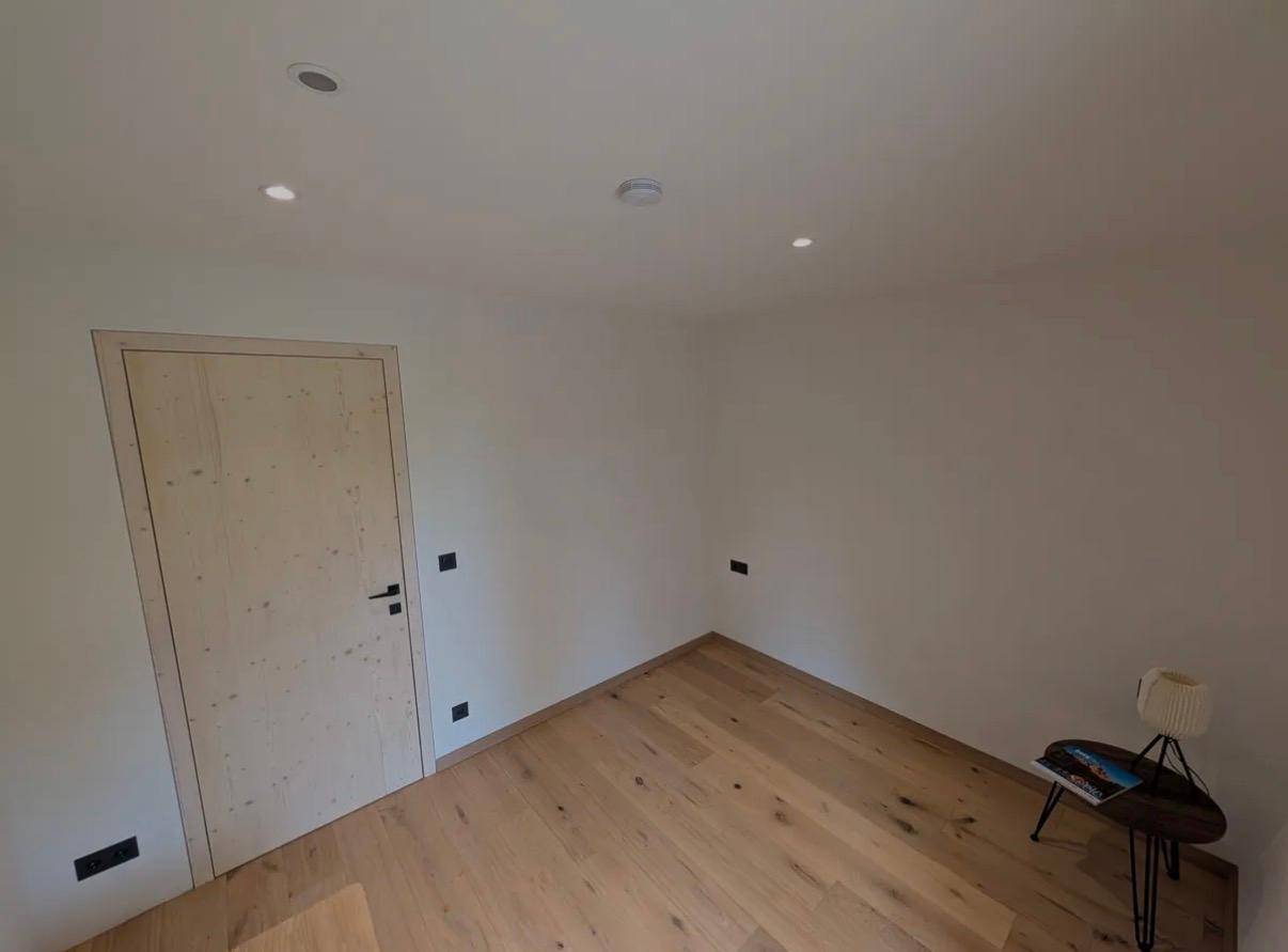 Leeres Zimmer mit hellem Holzboden, weiß gestrichenen Wänden und Einbaustrahlern.