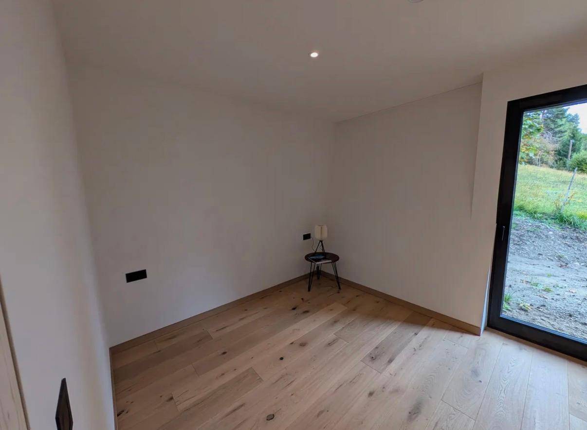 Helles Schlafzimmer mit Holzboden und Zugang zu einem Außenbereich, minimalistisch eingerichtet.