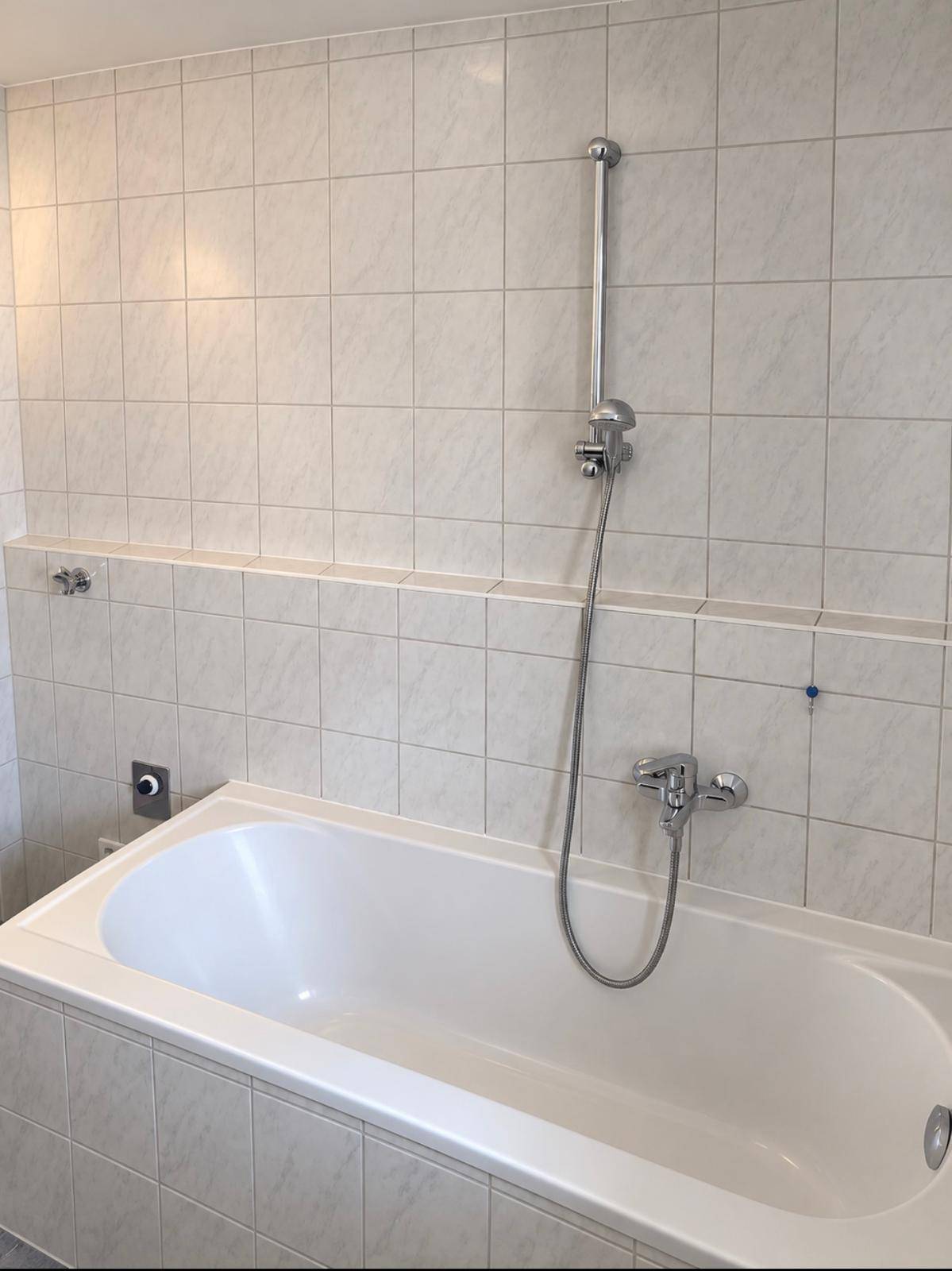 Helles Badezimmer mit Badewanne und weißen Fliesen an Wänden und Boden.