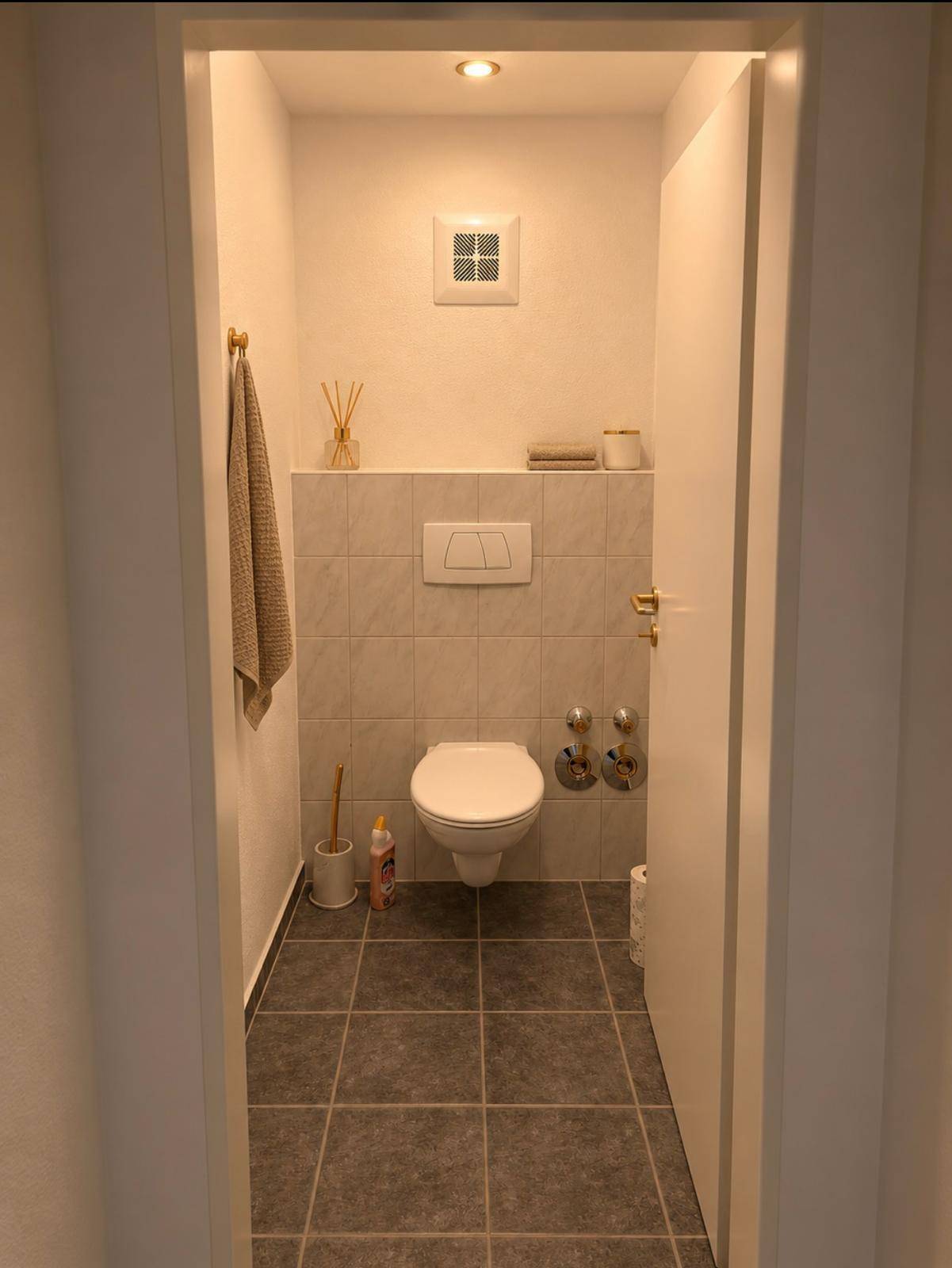 Modernes Gäste-WC mit Wand-WC, Fliesenboden und integriertem Lüfter.