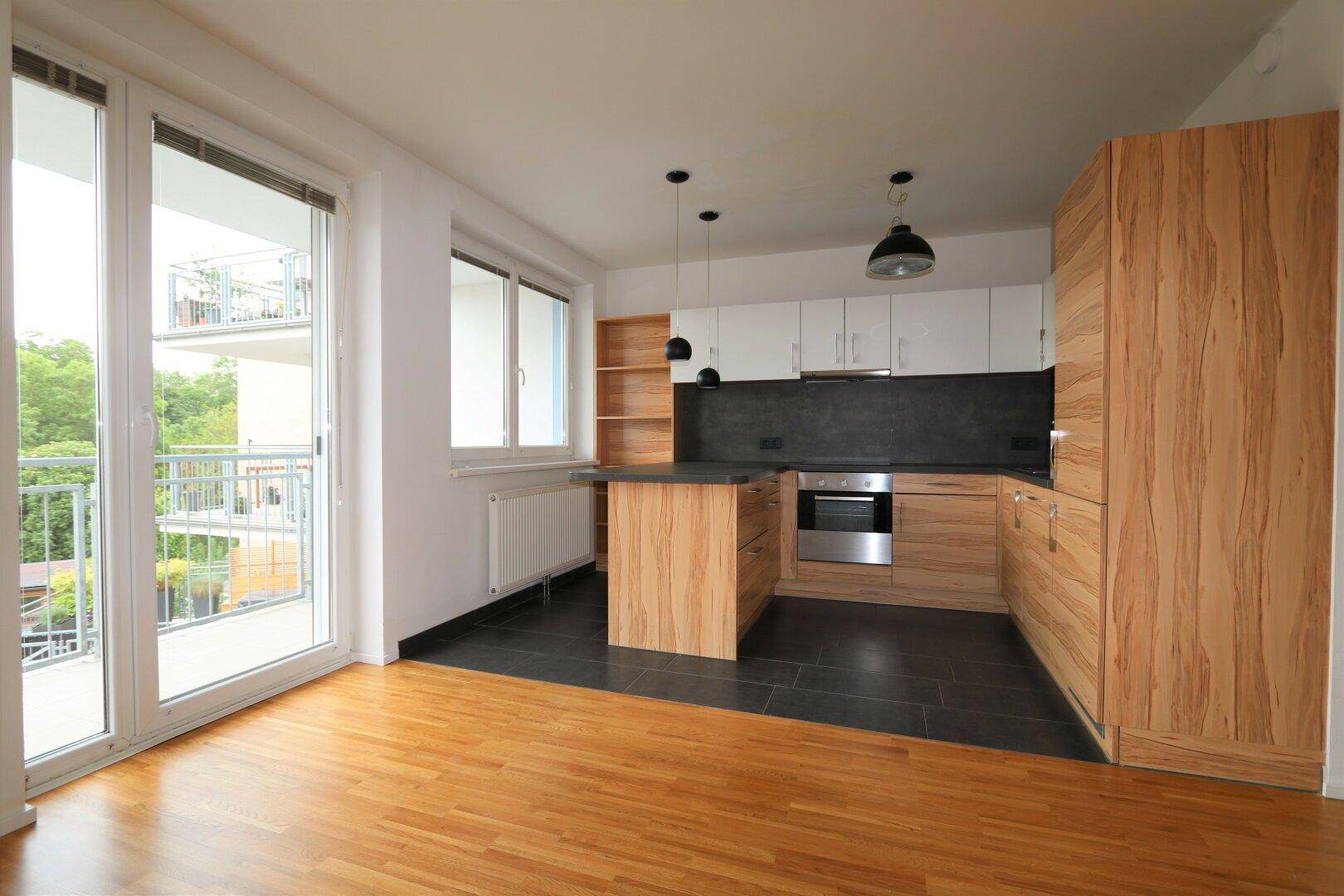 Wohnzimmer mit offener Küche und Zugang zum Balkon