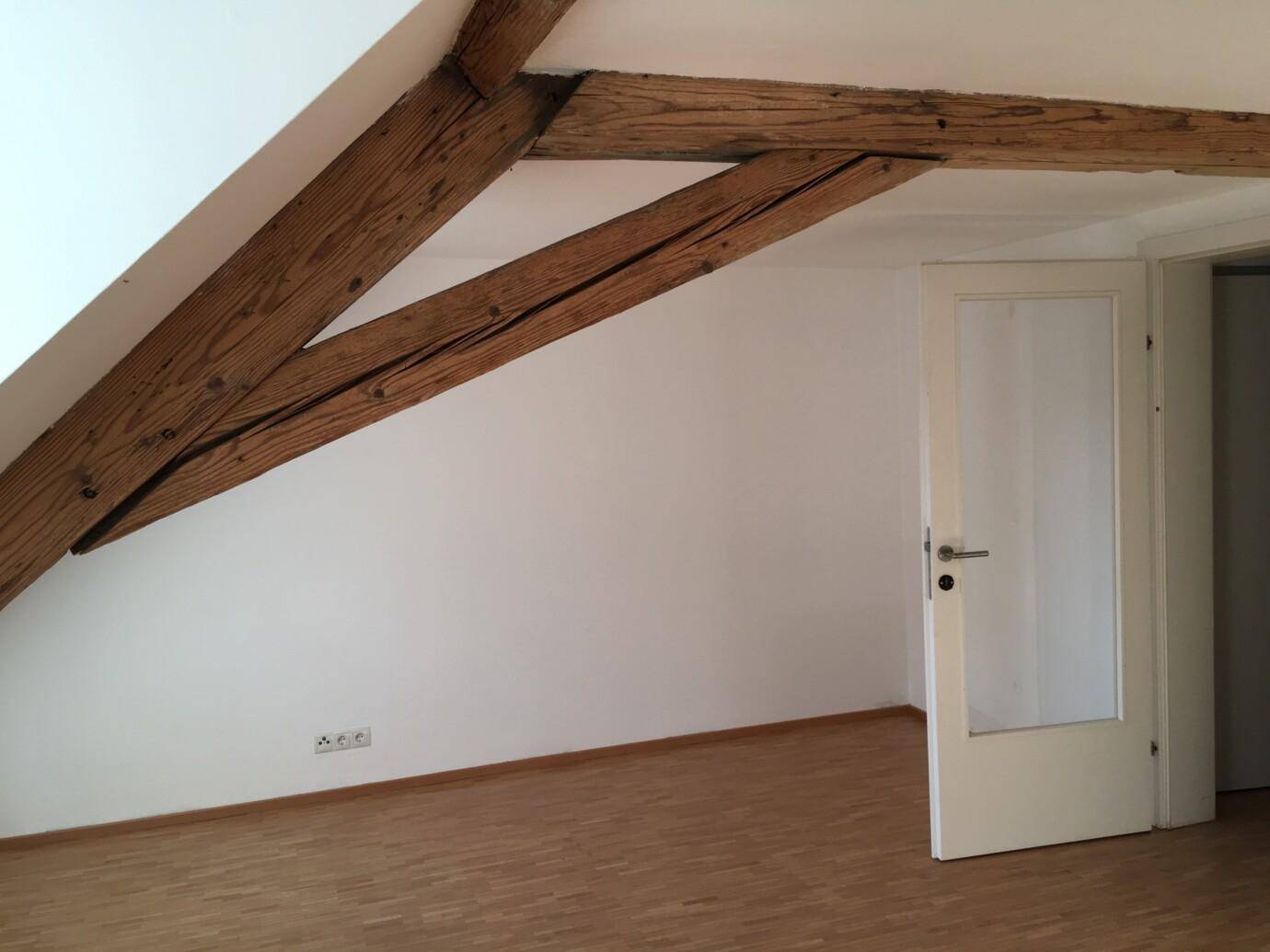Dachboden mit Dachschräge, leerer Raum mit Holzboden und Tür in anderen Raum